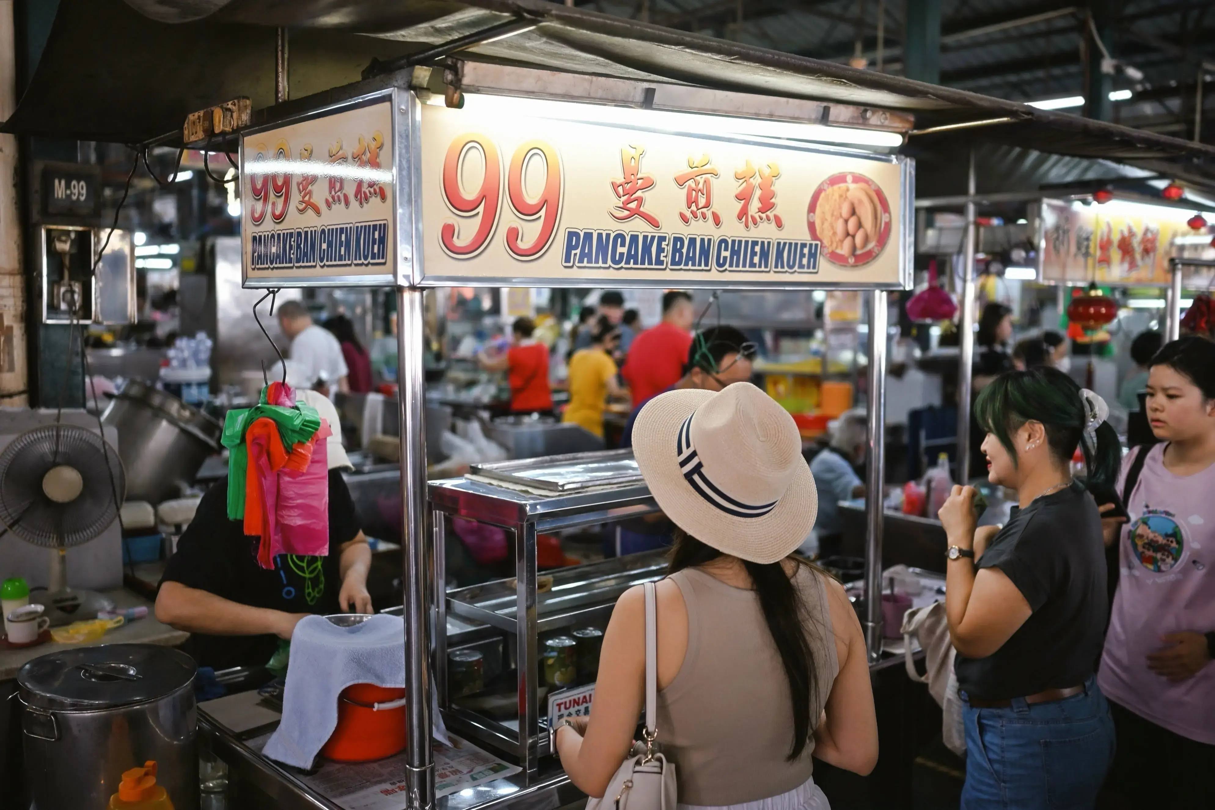 Street food stall in Penang's hawker center, featuring a sign for 99 Pancake Ban Chien Kueh